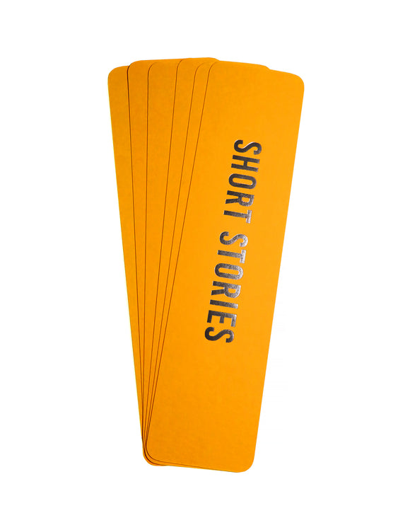 A fanned stack of rich marigold yellow  vertical bookmarks that reads SHORT STORIES in gunmetal silver foil embossed text.