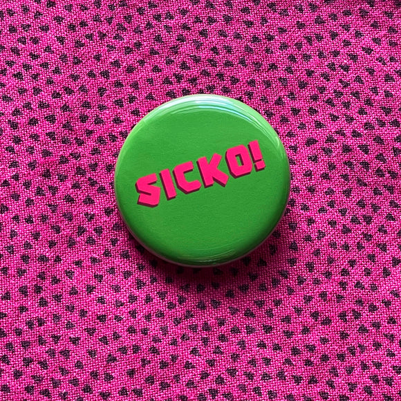 Round rich green pinback button reads SICKO! in hot pink text. Pinned to a vintage pink shirt with teeny tiny triangles