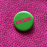 Round rich green pinback button reads SICKO! in hot pink text. Pinned to a vintage pink shirt with teeny tiny triangles