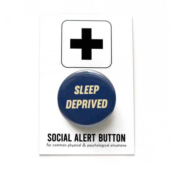 Round navy blue pinback button that reads SLEEP DEPRIVED in cream slanted text. Pinned to a Social Alert Button backing card.