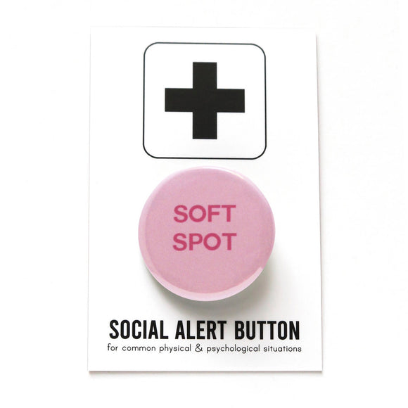 Round light pink pinback button that reads SOFT SPOT in dark pink. Pinned to a Social Alert Button backing card.