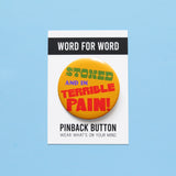 A round yellow-orange pinback button that reads STONED AND IN TERRIBLE PAIN! in green. purple & red text.  Button is on a Word For Word branded backing card that says Wear What's On Your Mind