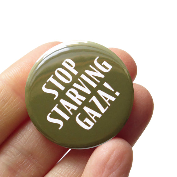 A round olive green pinback button that reads STOP STARVING GAZA! in white text. The button is held in a hand.