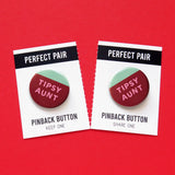 Two pinback buttons that look like red wine sloshing in a round cup with a mint great background.  In the red white color it reads: TIPSY AUNT in pink. Both buttons are on a backing card that splits in half at the perforation, a Pefect Pair, Tear & Share!