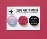 A Social Alert Buttons backing card with 3 pinback buttons attached, reading: Support Trans Kids, Bodily Autonomy Is a Human Right, Trans Rights are Human Rights, in various shades of pink, blue and black.