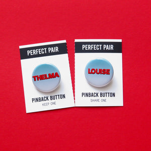 Two pinback buttons separated by a perforated line to tear & share. Button the left reads THELMA, button on the right reads LOUISE. Both buttons have a pale teal to white ombre with red text. On red background.