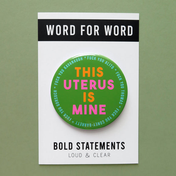 Big 3 inch shiny olive green pinback button with bright orange and hot pink chunky san serif text that reads: This Uterus is Mine. Smaller text in a light blue runs in a circle around the permitter that says Fuck You Alito, Fuck You Thomas, Fuck you Coney-Barrett, Fuck you Gorsuch, Fuck you Kavanaugh