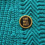 Round enamel pin that says TIME WILL PASS on the lapel of a brown striped tweed blazer.