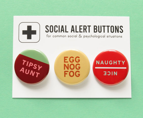 3 round pinback buttons lined up on a SOCIAL ALERT BUTTONS backing card. Reading left to right: Tipsy Aunt in Burgundy and mint green, EGG NOG FOG  buttery cream & nutmeg brown & reversible NAUGHTY/NICE in bright red with mint green text. Buttons on card are on a mint green background.