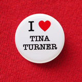 Round white pinback button with black serif test and a red heart. Text reads: I heart Tina Turner. Button is pinned to a red sweatshirt.