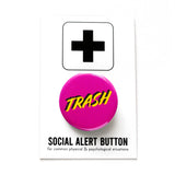 A round magenta pink pinback button that reads TRASH in a yellow font with a black drop shadow. Button is on a Social Alert Button backing card.