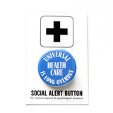 A round scrubs blue 1.25" pinback button that reads UNIVERSAL HEALTHCARE IS LONG OVERDUE in white text. Button is on a SOCIAL ALERT BUTTON backing card