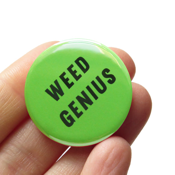 ound pinback button that says WEED GENIUS. Dark green text on a light green background. Button is held in a hand.