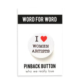 Round white pinback button that says I love women artists with a red heart. On a Word For Word backing card.