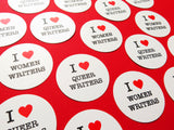 A bunch of round white stickers that reads I LOVE QUEER WRITERS & I LOVE WOMEN WRITERS, laid out over a red background. Love is represented by a heart on each sticker.