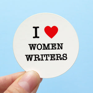 Round die-cut sticker that says I LOVE WOMEN WRITERS. The text is black with a red heart signifies the word love. The background is light blue.