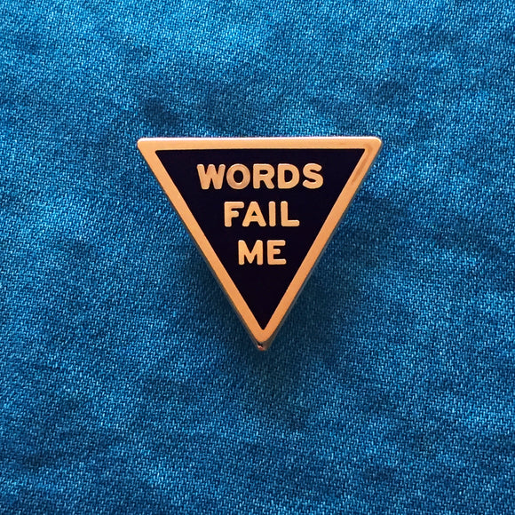Triangle shaped hard enamel copper & black enamel pin that says WORD FAIL ME . Pinned to blue denim.