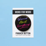 A round black  pinback button that reads WORRIED ABOUT EVERYTHING!  in purple, neon green & magneta pink text, in a retro 80's vibe.  Button is on a Word For Word branded backing card that reads Pinback Button, Wear What's On Your Mind