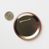 The back of a large metal pinback button, next to a quarter for size compare