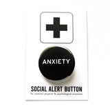 Round black pinback button that reads ANXIETY in white text. On a Social Alert Button backing card.