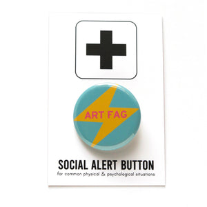 Round pinback button that says ART FAG. Pink text on a yellow lightening bolt on a teal background 