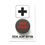 Round dark gray pinback button that says BAD MOOD in neon red text. On Social alert Button backing card.