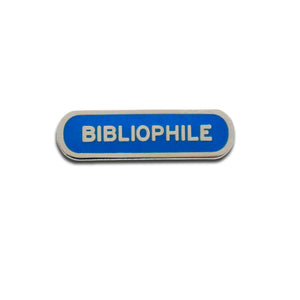 Capsule shaped enamel pin that says BIBLIOPHILE.  Silver text and outline on a royal blue enamel background.