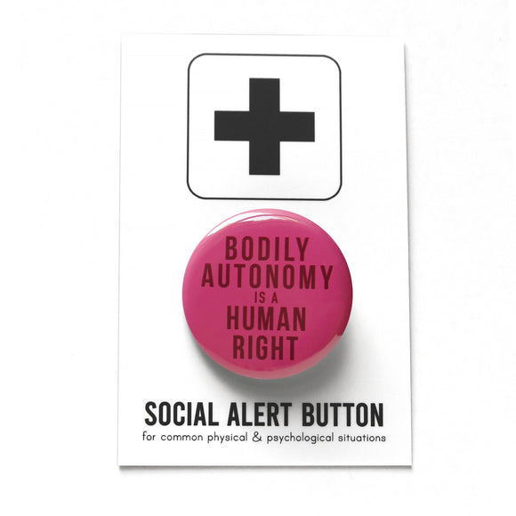 dark raspberry color pinback button that reads Bodily Autonomy Is A Human Right in dark red. On a Social Alert Backing Card