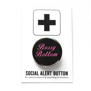 Round pinback button that reads BOSSY BOTTOM in bright pink text on a black background. Button is on a Social Alert Backing Card