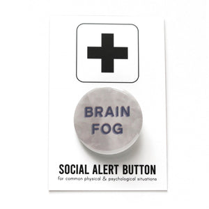 Round pinback button that says BRAIN FOG in blue-gray sans serif text on a cloudy gray background. Button is a on a white backing card that reads SOCIAL ALERT BUTTON on the bottom, with a black plus sign at the top.