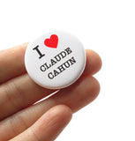 A round white pinback button that reads I LOVE CLAUDE CAHUN with love being a red heart. Held in a hand.