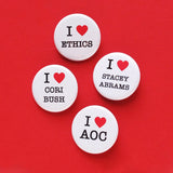 four white pinback buttons on a red background. One reads I love Ethics, second reads I love Stacey Abrams, third reads I love Cori Bush, fourth reads I Love AOC. The love is indicated by a red heart.  The text on each button is black serif font.