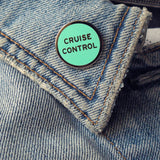 Round enamel pin that says CRUISE CONTROL on the lapel of a blue denim jacket.