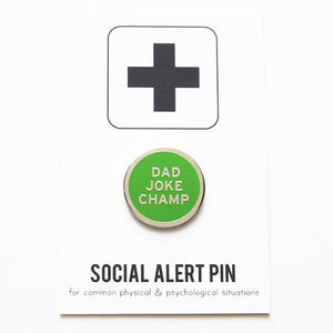 Round enamel pin the says DAD JOKE CHAMP on the lapel of a forrest green plaid flannel shirt