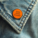 Round enamel pin the says DAD JOKE CHAMP on the lapel of a blue denim jacket.