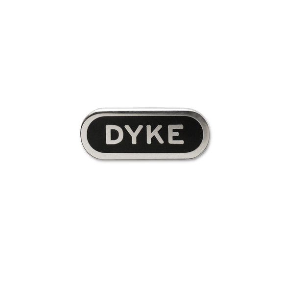Capsule shaped enamel pin that reads DYKE in silver colored text with an outline on a black enamel background.
