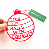 A round flat red holiday ornament that reads DECK THE HALLS WITH EQUALITY/ Red acrylic laser cut ornament with little tie and a Happy Holidays tag in green and white. 