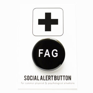 Product shot of a 1.25" pinback button on a cardboard social alert backing card.  The button has a black backround and white text that says FAG