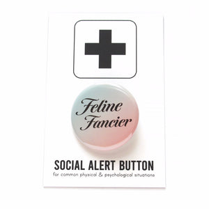 Shiny pinback button that is mint green to peachy-pink ombre with serif black text reading Feline Fancier. Button is on top of a white backing card with a black plus sign at the top, reading Social Alert Button at the bottom