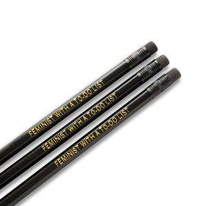 Three black pencils, with black ferrules and erasers, hot-foil pressed with the words FEMINIST WITH A TO-DO LIST in gold.