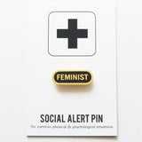 Capsule shaped enamel pin that says FEMINIST on a social alert pin backing card.