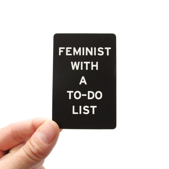 Rectangle sticker that says FEMINIST WITH A TO-DO LIST.  White text on a black background.