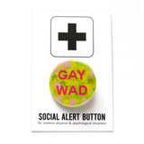 Round shiny pinback button with a yellow, green pink background which reads GAY WAD in dark pink san serif font. On a white backing card, black plus sign at the top. Below reads: Social Alert Button, with tiny text beneath it which says, for common physical & psychological situations  Edit alt text