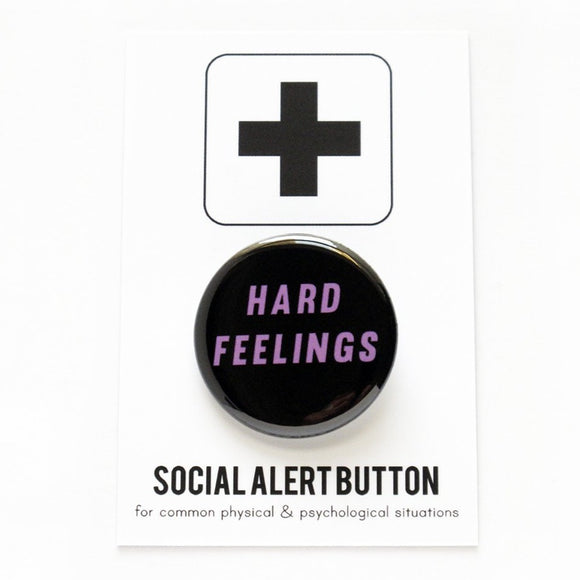 Round pinback button that says  HARD FEELINGS. Pink text on a black background.  Button is pinned to a Social Alert Button backing card.