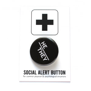 Round pinback button with black background which reads HE/THEY  on an angle in white text, in a san serif font. On a white backing card, black plus sign at the top. Below reads: Social Alert Button, with tiny text beneath it which says, for common physical & psychological situations