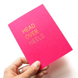 Hand holding a magenta Valentine's Day greeting card that says Head Over Heels