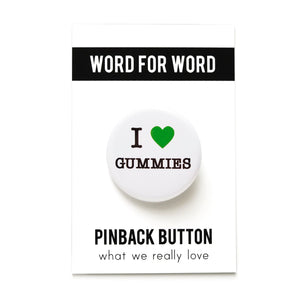 A round white pinback button that reads I LOVE GUMMIES, has a green heart representing love, and the rest of the phrase is in a classic serif font. The button is attached to a backing card which reads the brand WORD FOR WORD on the top in a black bar, and PINBACK BUTTON on the bottom, What We Really Love as the tagline