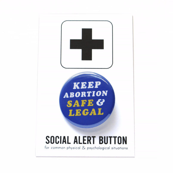 a white background with a white backing card that reads Social Alert Button at the bottom, and has a black plus sign at the top.  In the middle is a shiny dark bold blue pinback button with white and yellow text in a retro seventies font that reads, Keep Abortion Safe & Legal