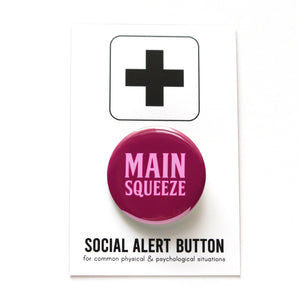 Round magenta-maroon pinback button that reads MAIN SQUEEZE in a light pink font. Button is on a Social Alert Button backing card.