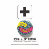 Round pinback button reading NON-BINARY.  The buttons has a  teal background and tiny black dots, a yellow ribbon comes in on the left reading NON, and a pink ribbon on the right comes in reading BINARY. The button is on a white card with a black plus sign at the top, at the bottom is reads Social Alert Button for common physical, psychological & social situations